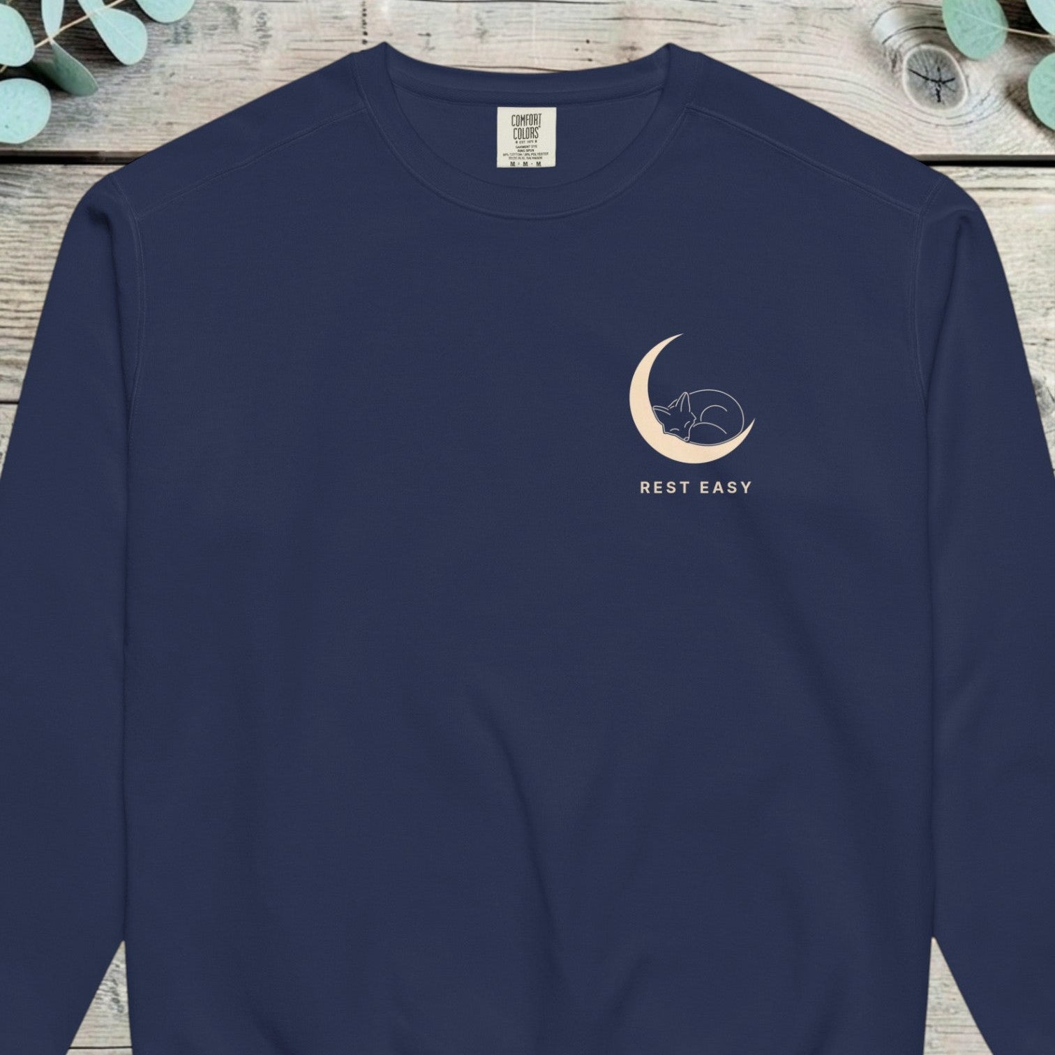 Small design of a fox curled asleep inside a crescent moon above the words REST EASY
