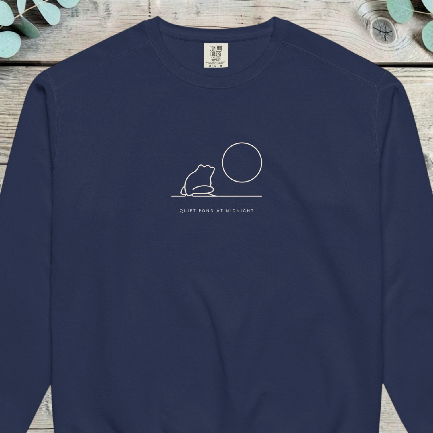Small single-line design of a frog sitting beside a full moon on a horizon line