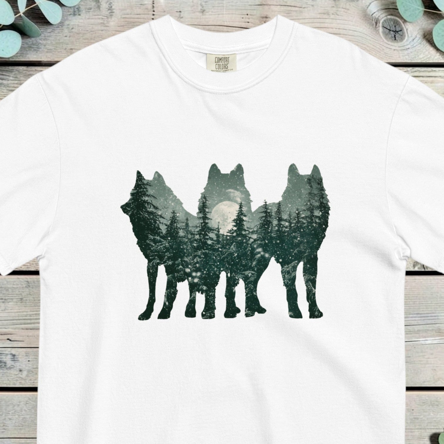 Three wolf silhouettes filled with a moonlit pine forest in a double exposure design