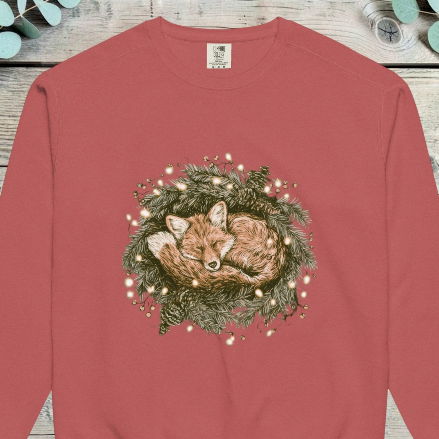 Fox curled up asleep inside a lit pine wreath on a sweatshirt