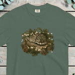 Tabby kitten asleep inside a pine wreath with small lights and pine cones
