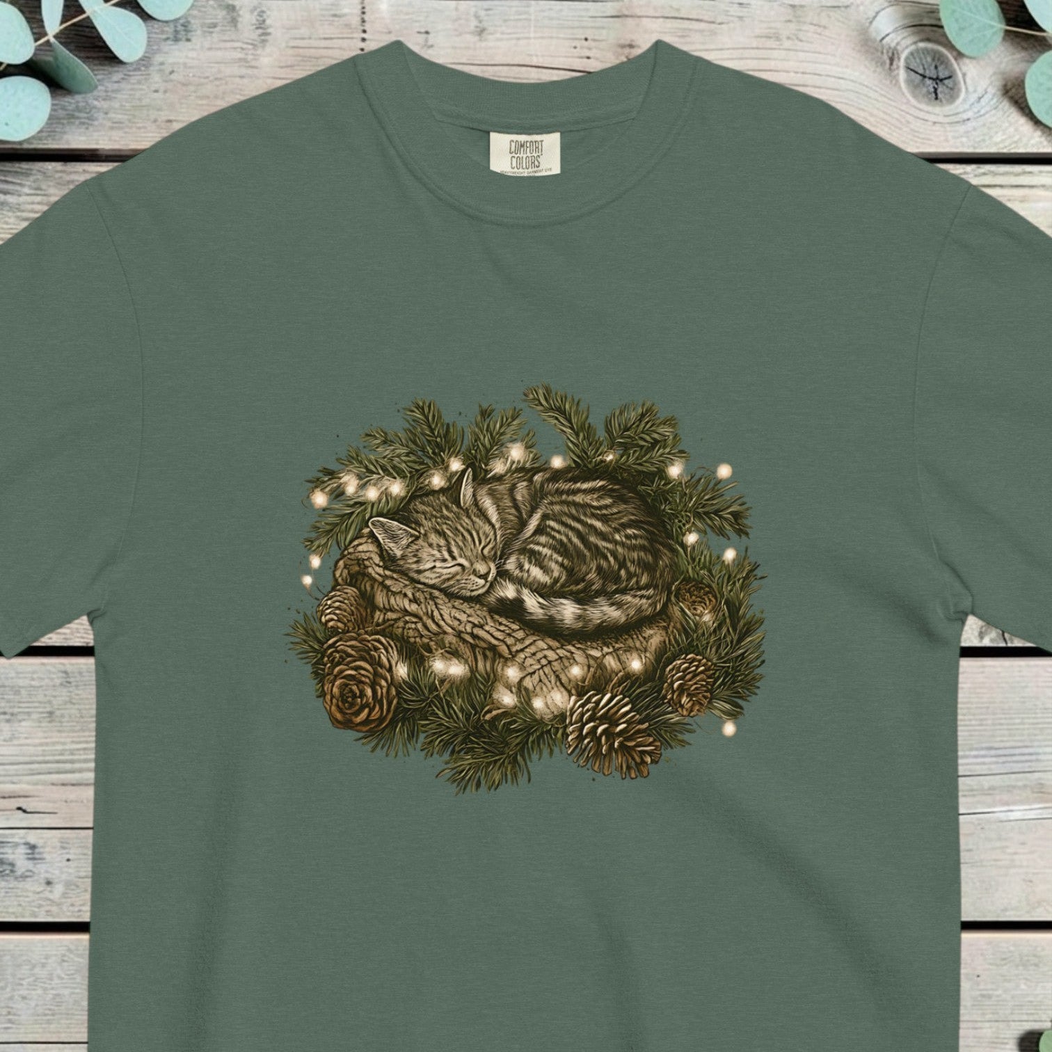 Tabby kitten asleep inside a pine wreath with small lights and pine cones