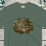 Tabby kitten asleep inside a pine wreath with small lights and pine cones
